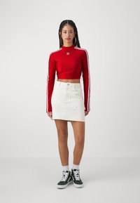 Κόκκινο κοντό μπλουζάκι με μακριά μανίκια και λευκές ρίγες, λευκή τζιν φούστα, πράσινα sneakers με ψηλή μπότα και λευκές κάλτσες μέχρι τον αστράγαλο.