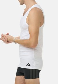 White tank top in cotton fabric with a deep V-neckline, paired with black fitted shorts featuring a subtle textured pattern and side stripes.