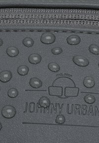 Un materiale grigio testurizzato presenta goccioline in rilievo e un logo impresso "JOHNNY URBAN" con un design minimalista. Chiusura con zip nella parte superiore.
