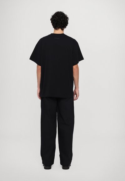 T-shirt en coton noir à manches courtes, coupe décontractée et col rond, associée à un pantalon noir large, vue de dos sur fond clair.