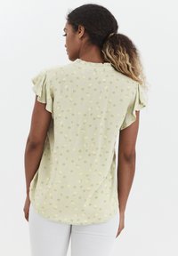 Hellgrüne Bluse mit floralen Mustern in Lila und Beige. Besitzt kurze Rüschensch sleeves und einen abgerundeten Saum. Weicher Stoff.