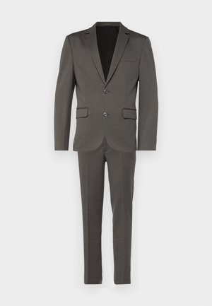 Costume gris comprenant une veste ajustée avec des revers en cran et une poche poitrine simple, associée à un pantalon slim.