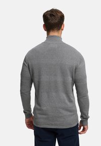 Grå genser med ribbestrikket hals, strukturert strikkemønster og horisontale striper. Lange ermer og tettsittende silhuett.