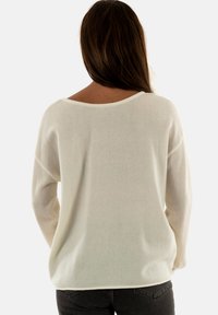 Maglione leggero di colore crema con una vestibilità ampia, scollatura larga e maniche lunghe, caratterizzato da una texture morbida e dettagli minimi.