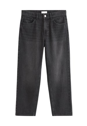 Dreng står iført en ensfarvet hvid t-shirt, løse sorte jeans og hvide sneakers mod en ensartet lys baggrund.