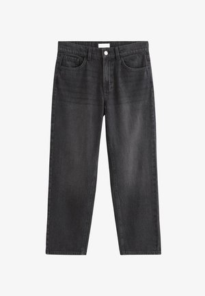 Dreng står iført en ensfarvet hvid t-shirt, løse sorte jeans og hvide sneakers mod en ensartet lys baggrund.