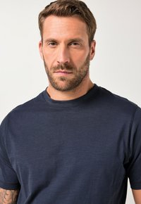 Námořnická modrá tričko s kulatým výstřihem vyrobené z měkké, texturované látky. Krátké rukávy a volný střih s minimem švů pro čistý vzhled.
