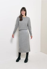 Ensemble en tricot gris en deux pièces composé d'un pull à col rond à coupe décontractée et d'une longue jupe, associé à des bottes noires à lacets. Texture lisse.