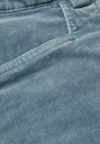 Vaaleansininen korduroypäällinen, jossa on pystysuoria uria, varustettuna ommellulla taskulla ja sileällä pinnalla. Lähikuva, joka korostaa yksityiskohtia.
