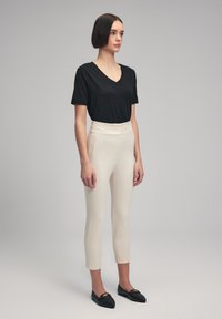 Svart v-hals t-shirt, krämfärgade högmidjade smala byxor och svarta loafers med gyllene accenter. Slät tyg, minimalistisk design.