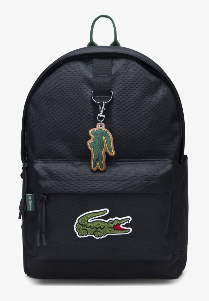 Schwarzer Rucksack mit einer Vordertasche, versehen mit einem grünen und weißen gestickten Logo und einem grünen Schlüsselanhänger in Form eines Krokodils.