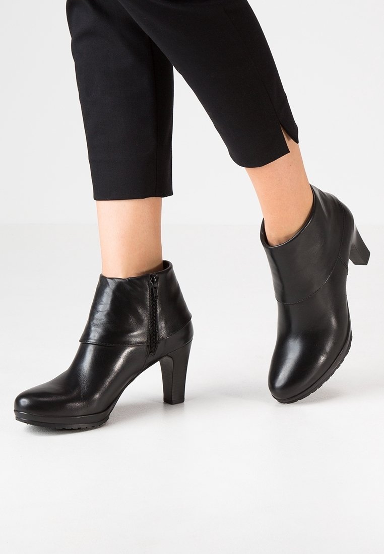 Bottes courtes en cuir noir avec fermeture éclair, dotées d'un talon haut, d'une texture lisse et d'un design incurvé en haut. Adaptées pour une tenue formelle.