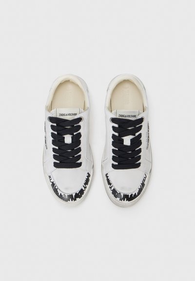 White leather sneakers with black laces, featuring a graphic black pattern on the toe cap and branded tongue. Smooth texture with a low profile.
