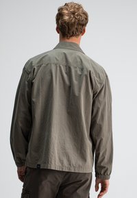 Olijfgroene oversized jack met een kraag, elastische manchetten en een rechte snit. Soepele textuur, casual ontwerp en subtiele merkdetail.