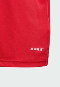 Rød træningsskjorte med glat stof og en micromesh-struktur samt et hvidt "AEROREADY" logo nær kanten.