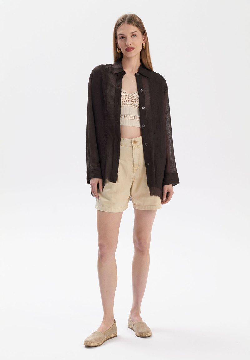 Black, lightweight, button-up shirt with a textured fabric, paired with a knitted cream crop top and beige shorts, completed with beige espadrilles.