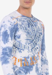 Langärmliges Batikshirt in Blau und Weiß, mit orange- und weißem Drucktext, Rundhalsausschnitt und weichem Baumwollmaterial.