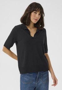 Zwarte polo met korte mouwen, v-hals ontwerp, gebreide textuur en een geribbelde zoom. Gepaard met blauwe denim jeans.
