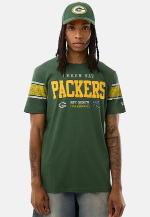 Person, die eine grüne Green Bay Packers Kappe und ein grünes T-Shirt mit gelben Streifen und NFL-Teamlogos trägt.