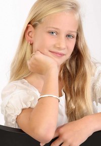 Zilveren armband om de pols van een kind, gecombineerd met creolen. Draagt een lichtgekleurde blouse met gerimpelde mouwen, een soepele textuur en natuurlijk haar.
