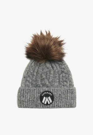Grå strikket beanie med kabeldesign, prydet med en brun faux fur pom-pom ovenpå og et sort rundt logo-patch mærket "SUPERDRY."