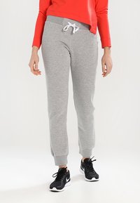 Graue Sweatpants mit elastischen Bündchen und Kordelzugbund, die eine sanfte Textur aufweisen. Kombiniert mit schwarzen Sportschuhen und einem roten Oberteil.