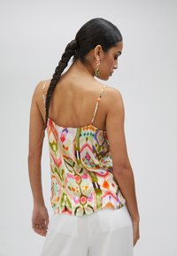 Camisole di seta multicolore con un motivo geometrico, spalline sottili e regolabili, e una vestibilità ampia, indossata con pantaloni bianchi.