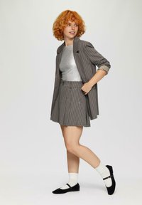 Grijs gestreepte blazer over een zilveren top, gecombineerd met een bijpassende grijs gestreepte rok. Zwarte ballerina's met een bandje, witte sokken. Soepele texturen.