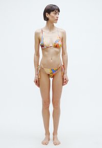 Bikini szett színes absztrakt mintával, sima anyagból készült. A felső háromszög alakú kosarakkal és vékony pántokkal rendelkezik, az alsó pedig oldalán megkötős.