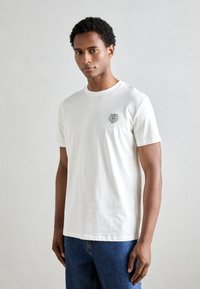 Camiseta de algodón blanca de manga corta con un gráfico circular de un león en negro en el pecho, con un cuello redondo clásico y un ajuste relajado.
