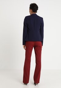 Chaqueta azul marino a medida con cuello alto, diseño ajustado y textura suave, combinada con pantalones rectos color burdeos.