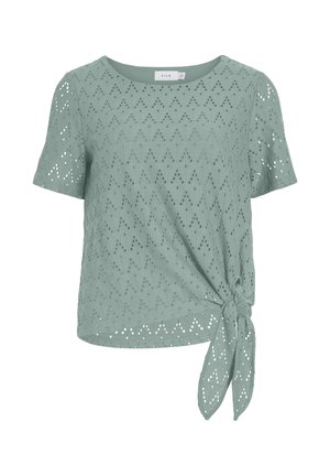 Blouse vert clair à manches courtes en tissu ajouré avec un détail de nœud sur le côté de l'ourlet.