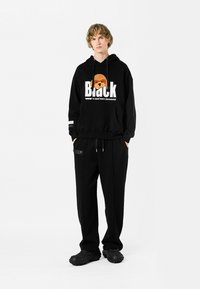 Sudadera negra con un gráfico de perro y texto blanco, combinada con pantalones negros y zapatos texturizados negros. Ajuste cómodo y casual.