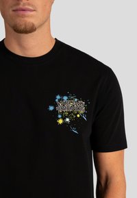 Zwarte T-shirt met korte mouwen, voorzien van een kleurrijke grafische print met spettereffecten en de tekst "WRONG FRIENDS" op de linkerkant van de borst.