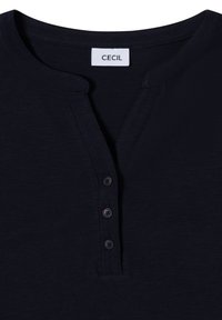 Tummansininen puuvillainen henley-paita, jossa on pyöreä kaula-aukko, kolme nappia edessä ja etiketti, jossa lukee "CECIL". Pehmeä rakenne ja rento muotoilu.