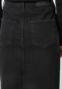 Črna denim krila s srednjo dolžino, dvema zadnjima žepoma in šivom na sredini. Material se zdi trden z teksturirano površino.