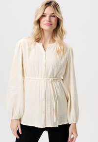Helle cremefarbene Bluse mit langen Ärmeln, strukturiertem Stoff, durchgehender Knopfleiste und einem Bindegürtel in der Taille. Weiche, leicht oversized Passform.