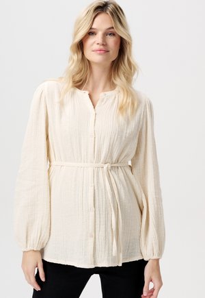 Helle cremefarbene Bluse mit langen Ärmeln, strukturiertem Stoff, durchgehender Knopfleiste und einem Bindegürtel in der Taille. Weiche, leicht oversized Passform.