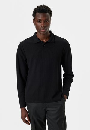 Camisa polo negra de manga larga con un diseño de punto texturizado, que cuenta con un collar clásico y un ajuste ligeramente entallado.