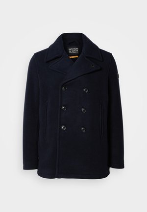 Marineblå ull pea coat med dobbeltknepping, stor skråkrage og to frontlommer. Har svarte knapper og skulderlapp.