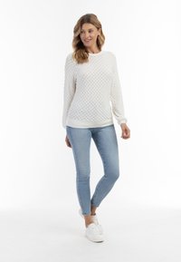 Maglione bianco a trama con maniche lunghe e collo rotondo, abbinato a jeans skinny blu chiaro e sneakers bianche.