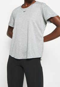 Szara sportowa koszulka z miękkiego, fakturowanego materiału. Posiada okrągły dekolt oraz małe czarne logo Nike na piersi. Krótkie rękawy.