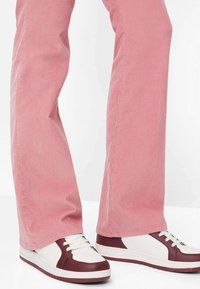 Pantalon en velours côtelé rose avec des nervures verticales, associé à des baskets plates blanches et bordeaux, à lacets sur le devant et bouts ronds.