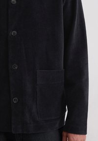 Marineblauwe corduroy jas met knoopsluiting, een borstzak en ribbeltextuur op de stof. Zacht, warm materiaal met een relaxte pasvorm.