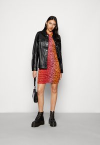 Casaco de pele preto, vestido com padrão vibrante em laranja e vermelho, e botas de combate pretas. Pequena bolsa preta com detalhes texturizados.