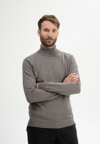 Hellgrauer Rollkragenpullover aus glattem Strickmaterial, mit gerippten Bündchen und Saum, kombiniert mit schwarzen engen Hosen.