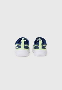 Chaussures de sport bleu marine et vert vif avec une tige en maille, un coussin au niveau de la cheville et une sangle Velcro ; semelles en caoutchouc blanc avec une adhérence texturée.