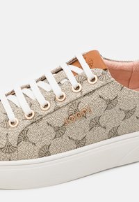 Beige patterned fabric sneaker with white laces and eyelets, tan leather accent on the tongue, and a white rubber sole. Features a logo.