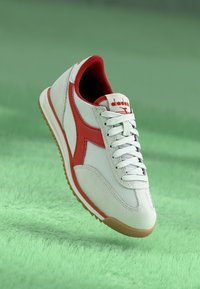 White athletic shoe with red accents and a mesh upper. Features laces, a padded collar, and a gum rubber sole.