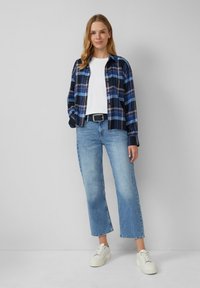 Lässiges Outfit mit einem karierten, blauen Button-up-Hemd, einem weißen T-Shirt, hellblauen Jeans und weißen Sneakers. Das Hemd hat kontrastierende Karomuster.